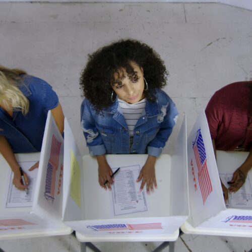 a birds-eye-view of a group of three people at ballot boxes, one in thought
