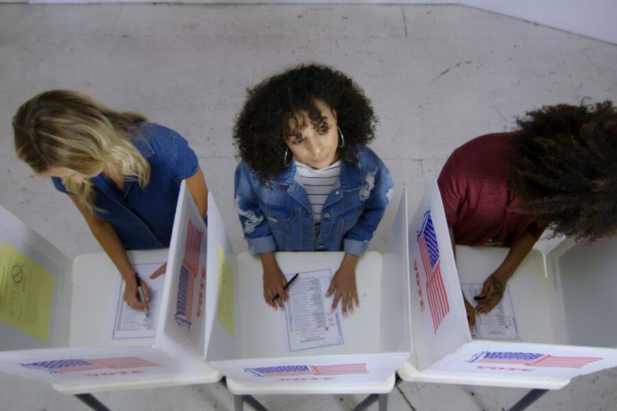 a birds-eye-view of a group of three people at ballot boxes, one in thought