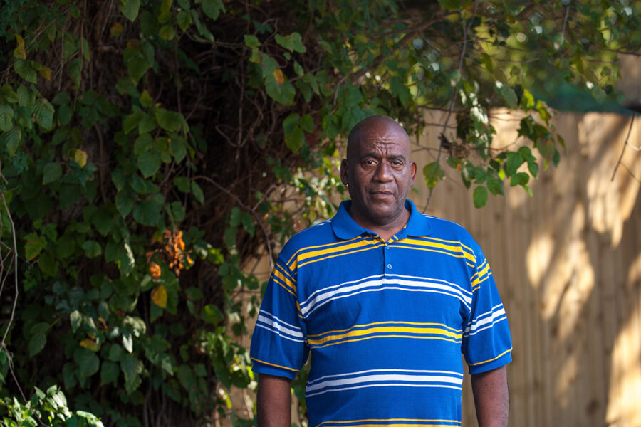 Houston client, Hervis, standing outside in the shade amongst greenery, in a striped polo and blue jeans