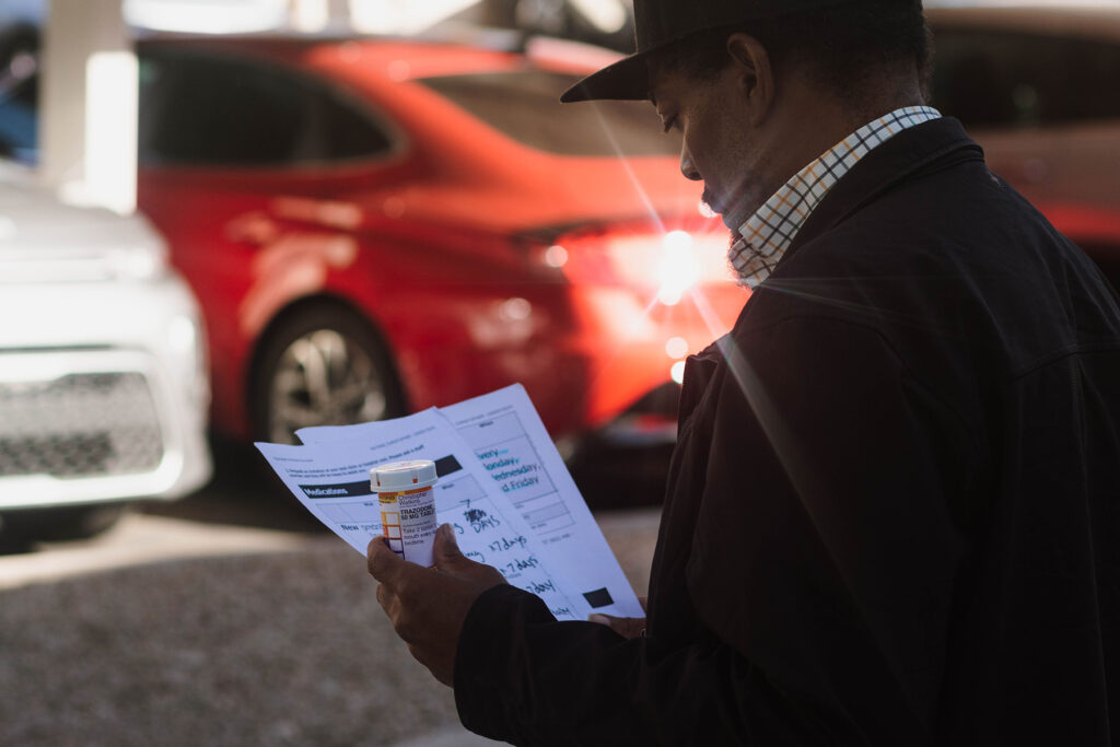 Phoenix client, Christopher, in a baseball cap outside looking over paperwork with a pill bottle