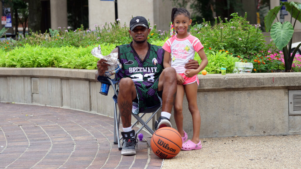 Bruce, a Louisville client, sitting outside in a baseball cap with a young girl and a basketball.