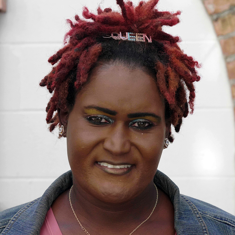 A woman with red dreadlocks on her head in front of a brick wall, advocating for trans rights in New Orleans.