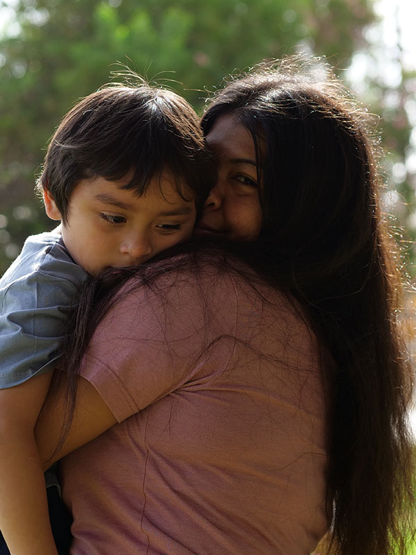 A mother holding her child, outside in the sun amongst trees