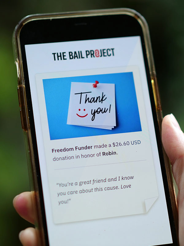A hand holding a cell phone; The Bail Project thanks them for their donation