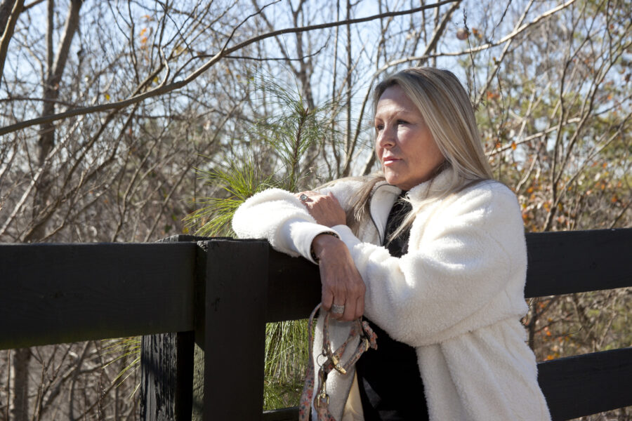 a woman leaning on a fence with her hand on her shoulder.