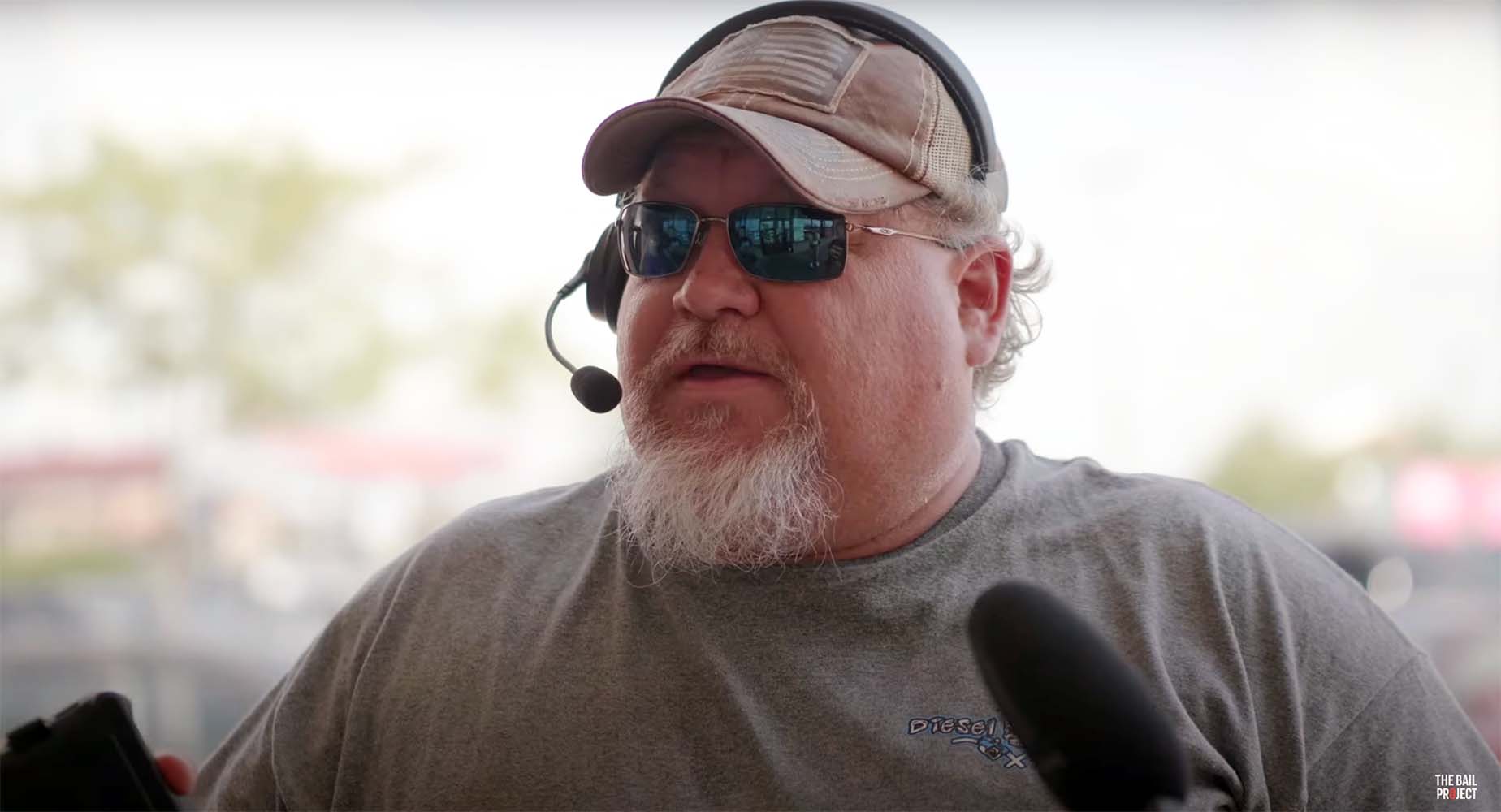 A bearded Kentucky resident wearing a headset and sunglasses speaking into a microphone