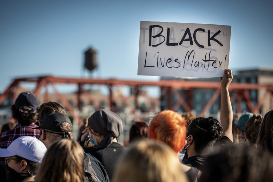 A black lives matter protest with a sign held up by a crowd.