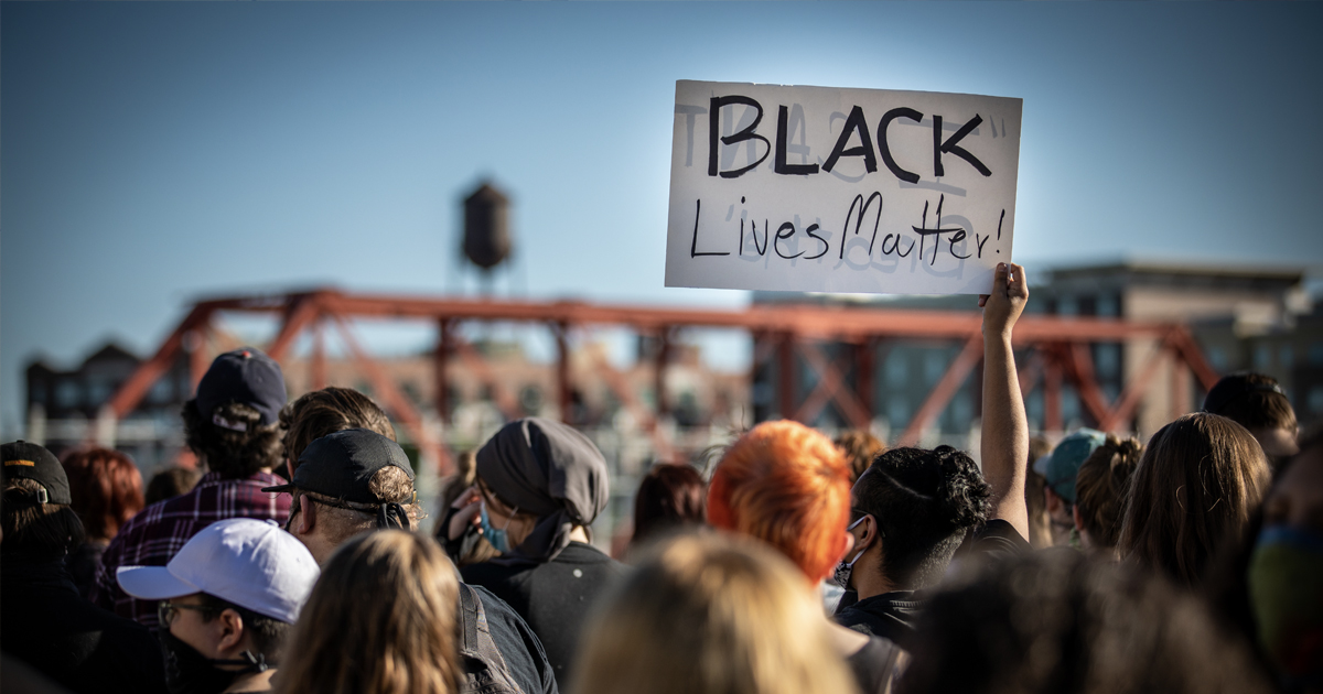 A black lives matter protest with a sign held up by a crowd.