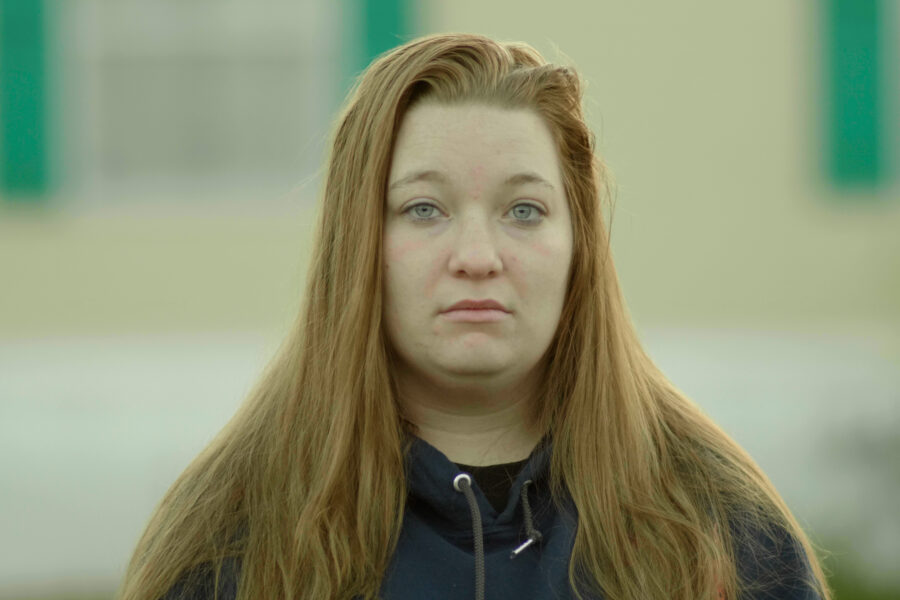 A red-haired woman impacted by the cash bail system looks at the camera.