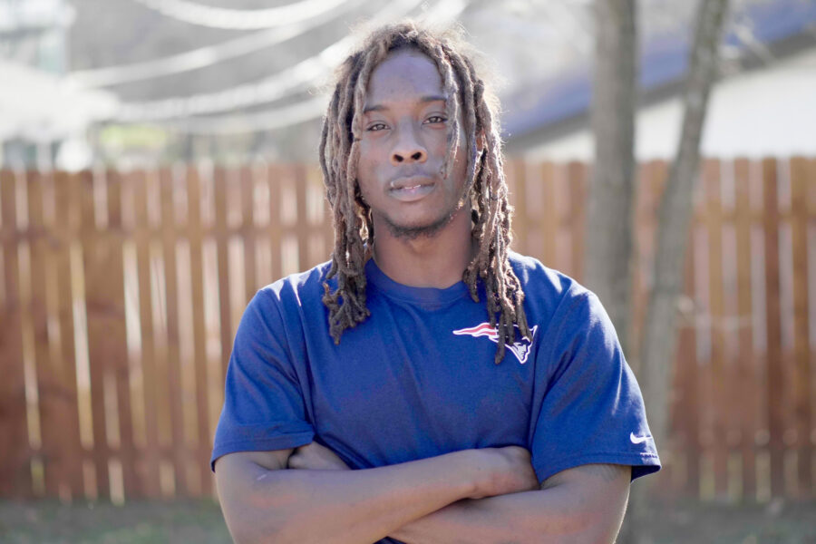 A man with dreadlocks standing in front of a fence with arms across his chest discusses racial disparities in the criminal justice system