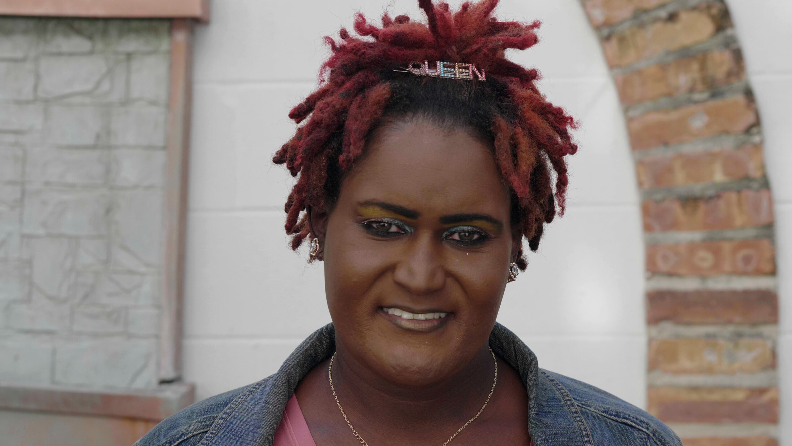 A woman with red dreadlocks on her head in front of a brick wall, advocating for trans rights in New Orleans.