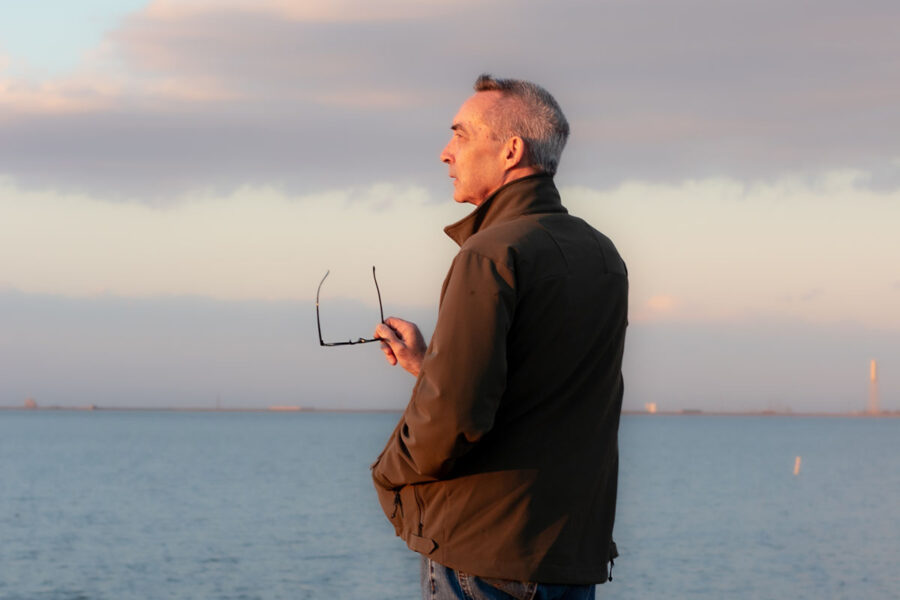 A man standing on a beach holding a pair of glasses.