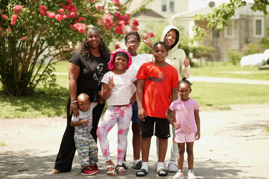 A family standing next to each other, in the sun amongst trees and homes