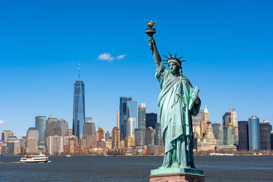 The statue of liberty stands in front of the NYC skyline.