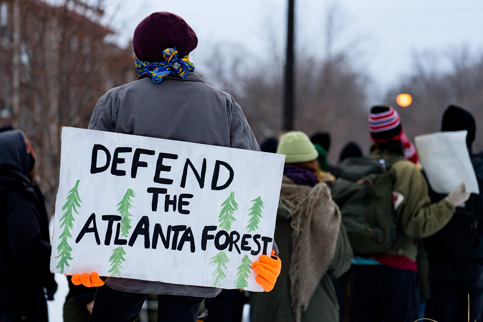 a group of protestors, with one holding a sign that says "defend the Atlanta forest".