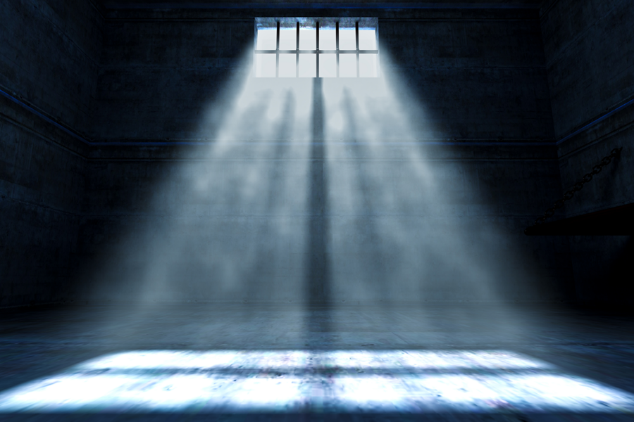 A ghostly light falls through a small barred window in an empty jail cell