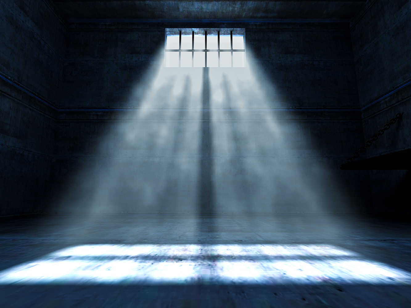A ghostly light falls through a small barred window in an empty jail cell