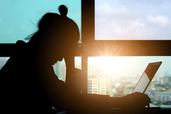 A woman sitting at her laptop, stressed, with sun rising through the window
