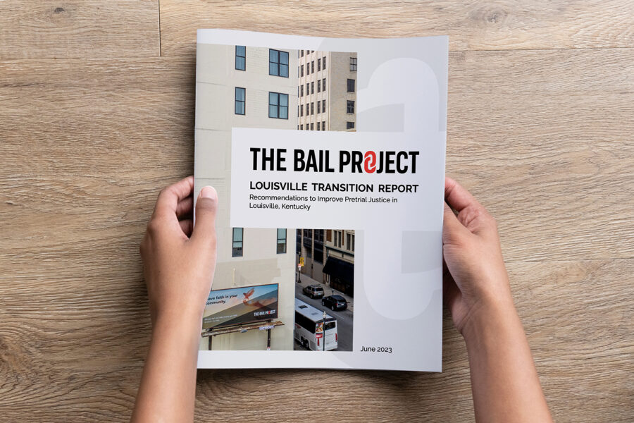 Hands holding the "Louisville Transition Report" from The Bail Project, on a wooden table
