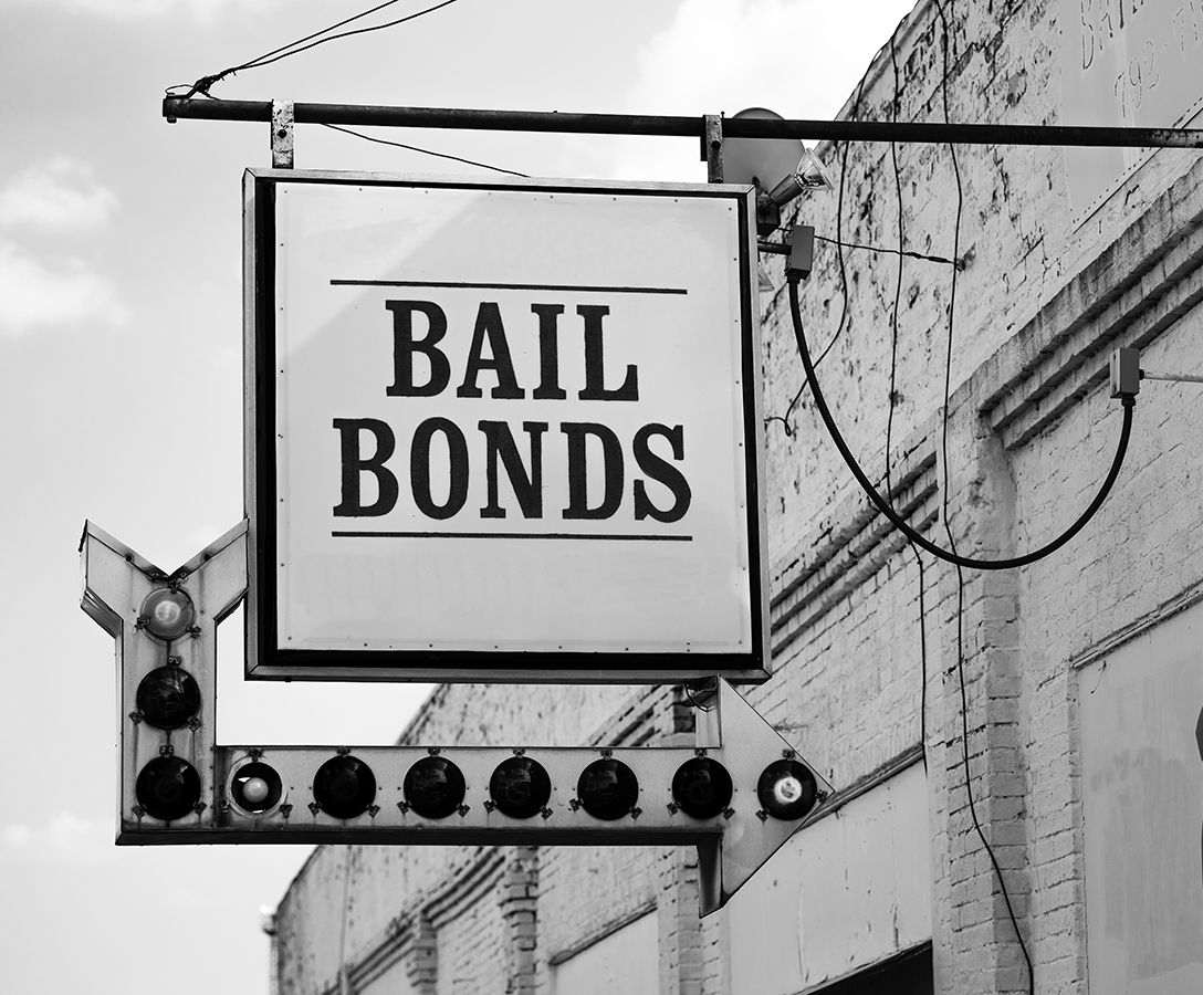 A rusty white bail bonds sign needs bulbs replaced but still points at the office entrance