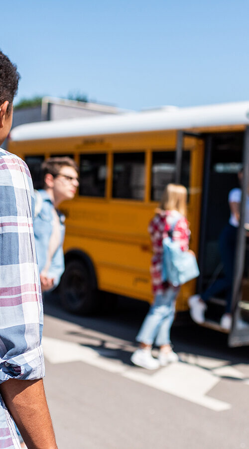 rear view of teen schoolboy walking to school bus with his classmates