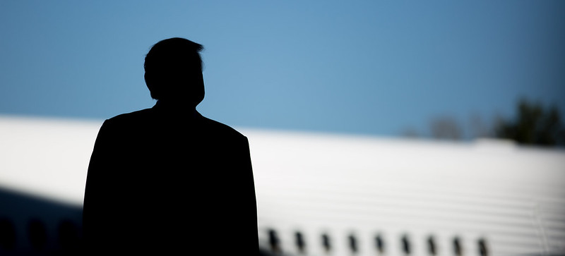 Donald Trump in silhouette, in front of a sky and airplane