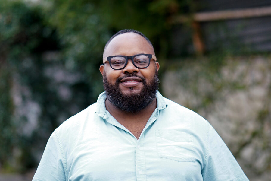 Clinton Washington in glasses and a button-up shirt smiling at the camera standing outside